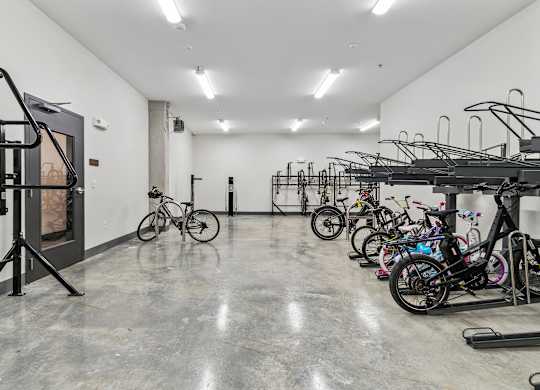 A room with a concrete floor and white walls is filled with bicycles.