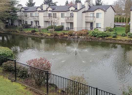 A fountain in the middle of a pond in front of a building.