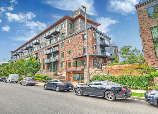 A street view of a multi-story building with cars parked in front.