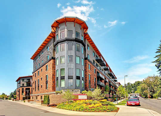 A red brick building with a curved corner and a red car parked in front.