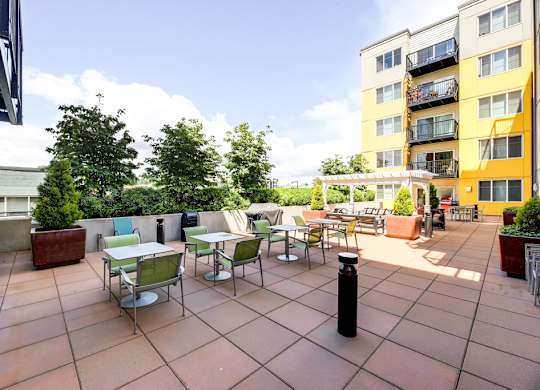 A patio with tables and chairs is surrounded by buildings.