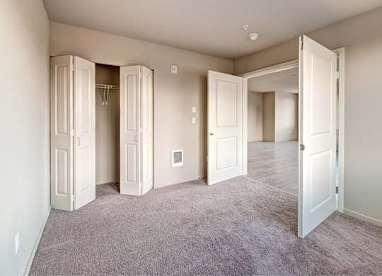 A room with a carpeted floor and white walls with a few open doors.
