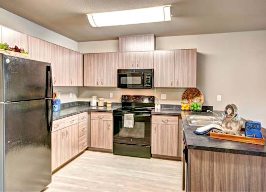 A kitchen with a black refrigerator and wooden cabinets.