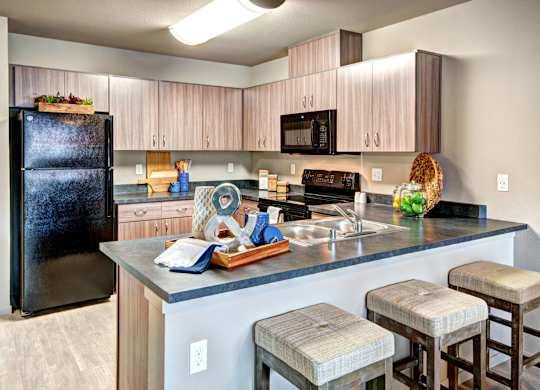 A kitchen with a black fridge, wooden cabinets, and a black stove top oven.