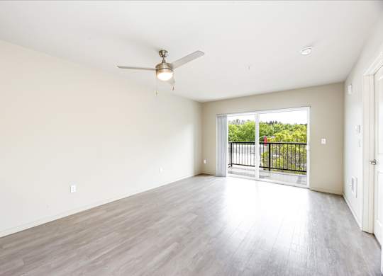 A spacious room with a ceiling fan and sliding glass doors leading to a balcony.