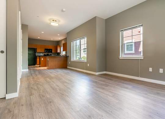 A spacious living room with wood flooring and a kitchen area in the background.