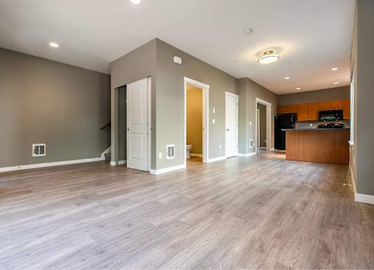 A spacious room with wooden floors and a kitchen area in the background.