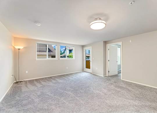 A spacious room with a carpeted floor and a window showing a view of other buildings.