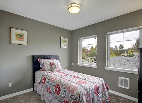 A bedroom with a bed, two windows, and two pictures on the wall.