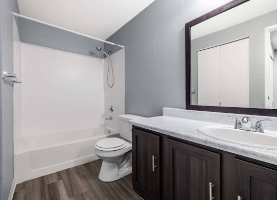 A white toilet sits in a bathroom with a white tub and a white sink.