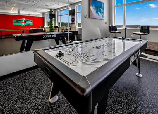 A black air hockey table in a room with a red wall and a window.