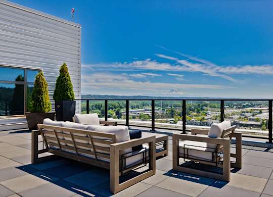 Two wooden chairs and a sofa on a patio overlooking a cityscape.