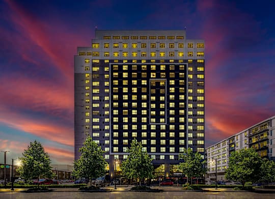 A tall building with many windows is lit up at dusk.