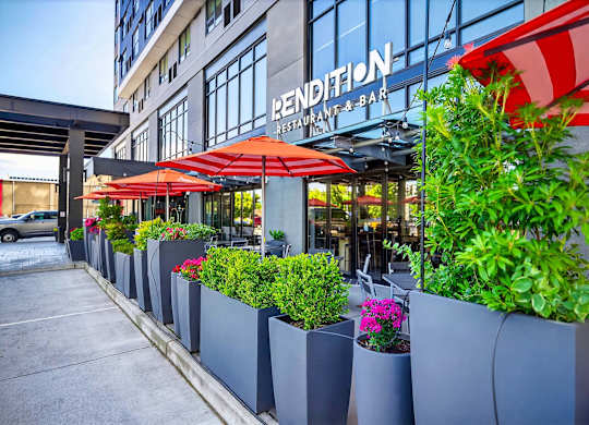 A row of grey planters with greenery and flowers in front of a building with a red and white striped awning.