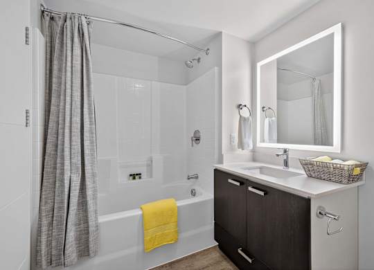 A bathroom with a white tub, sink, and a grey shower curtain.