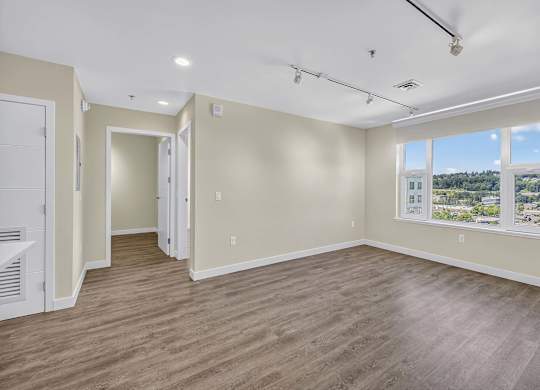 A spacious room with wooden flooring and a large window.