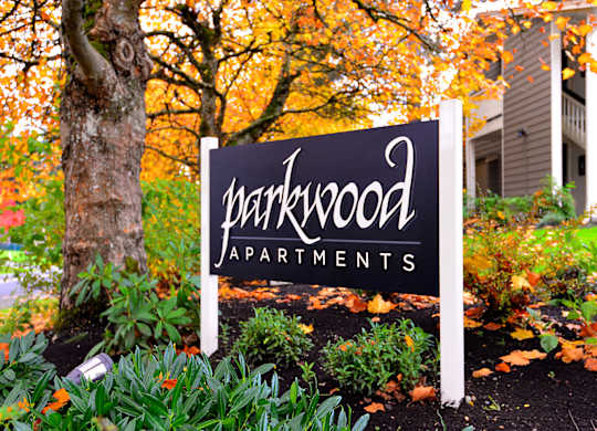 A sign for Parkwood Apartments is in front of a tree.