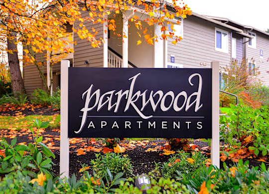 A sign for Parkwood Apartments is in front of a building.
