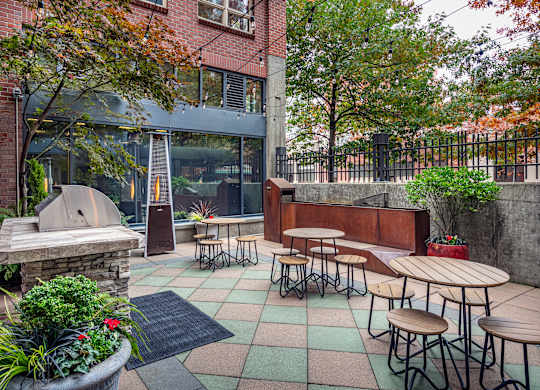 A patio with tables and chairs is surrounded by trees.