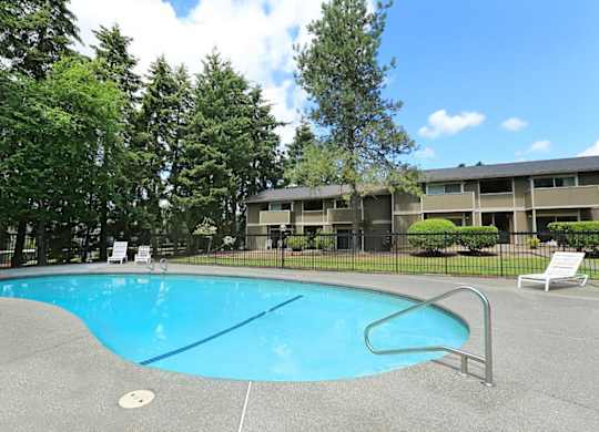 A swimming pool surrounded by trees and a building in the background.