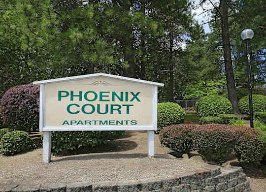A sign for Phoenix Court Apartments is displayed in front of a landscaped area.