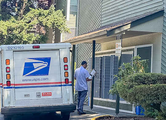 A mail truck is parked on the street in front of a house.
