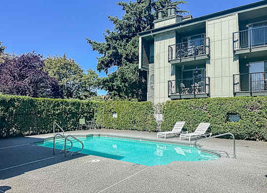 A pool with chairs and a building in the background.