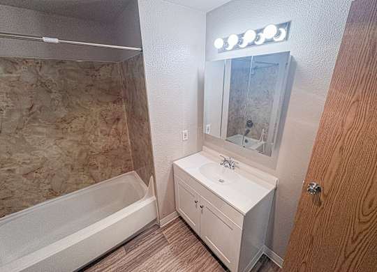 A small white bathroom with a sink, mirror, and bathtub.