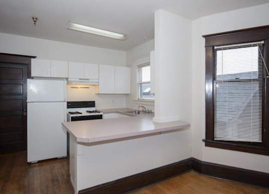 A kitchen with white appliances and a wooden floor.