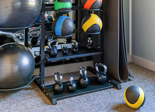 A black and silver exercise ball sits on the floor next to a black and silver weight rack.