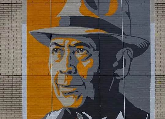 A mural of a man in a hat is painted on a brick wall.