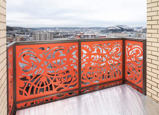 A balcony with a red railing and a view of a cityscape.