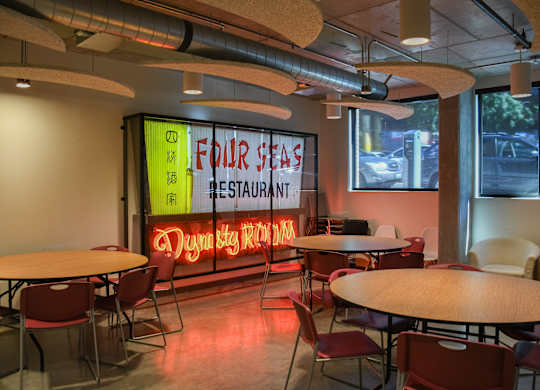 A restaurant with tables and chairs and a neon sign that says "Four Seas Restaurant".