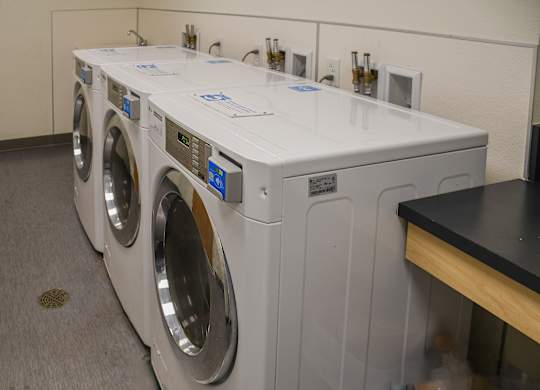 A row of white front load washing machines are lined up in a laundromat.