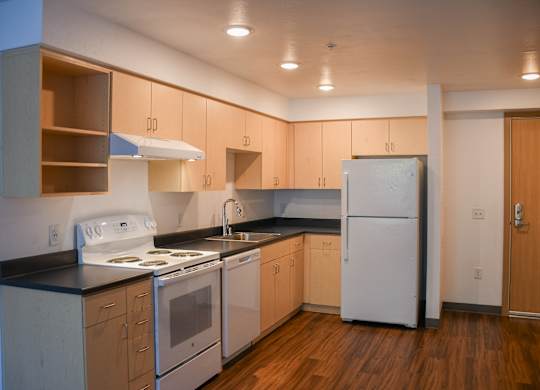A kitchen with a white stove top oven, white refrigerator, and wooden cabinets.