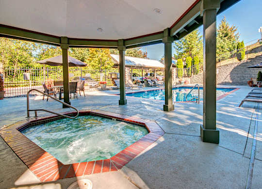A hot tub is surrounded by a pool and a patio area.