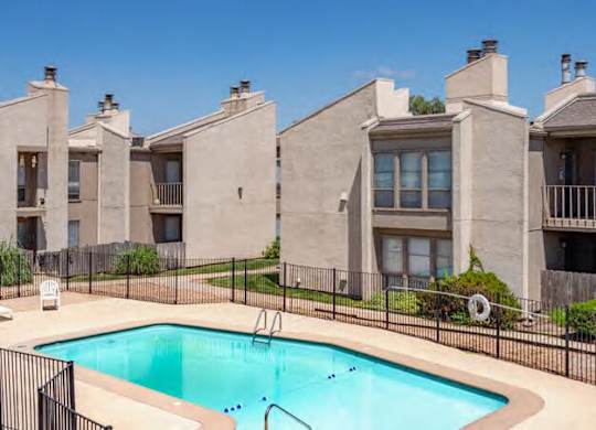 A swimming pool is surrounded by a black fence in front of a building.