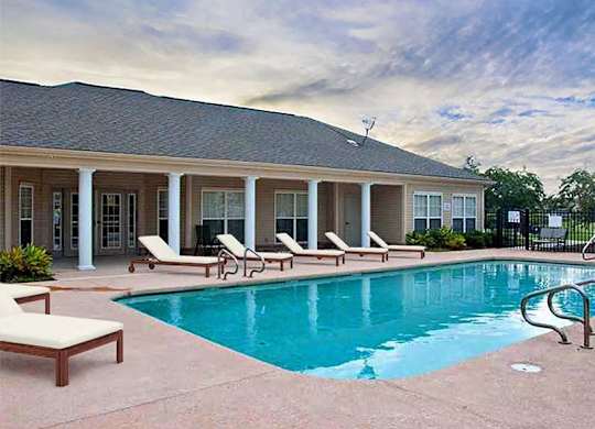 A pool area with sun loungers and a house in the background.