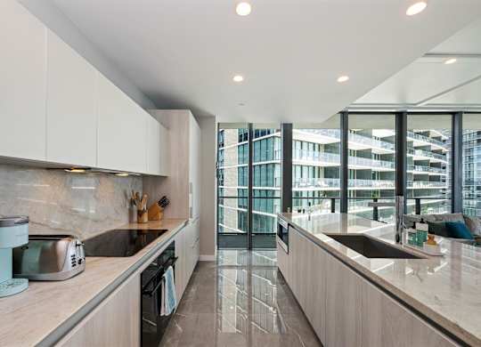 A modern kitchen with a marble countertop and a view of a cityscape through the windows.