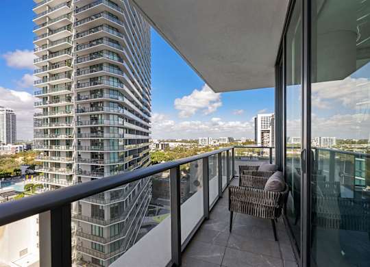 A balcony with a chair and a table overlooking a cityscape.