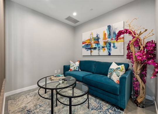 A living room with a blue couch and a painting on the wall.