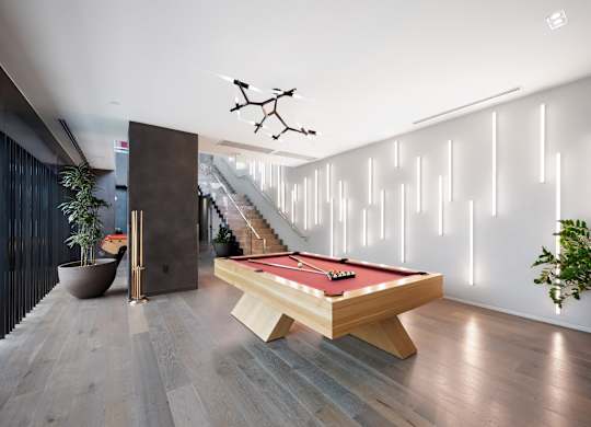 A pool table is in the middle of a room with a lighted wall behind it.