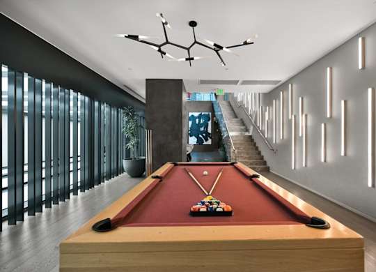 A pool table is in the middle of a room with a staircase in the background.