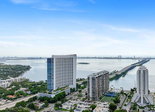 A cityscape with a large body of water in the foreground and a bridge in the distance.