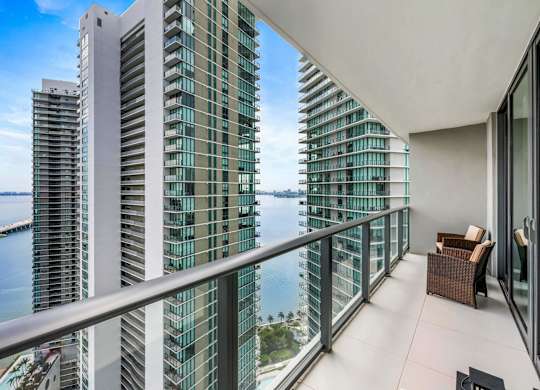 A balcony with a chair and a table overlooks a body of water.