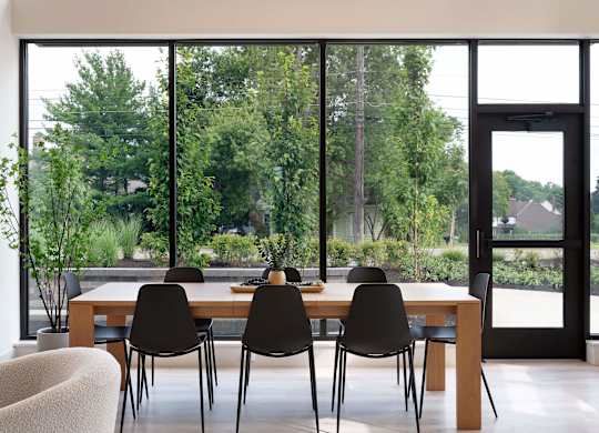 A modern dining room with a table and chairs in front of large windows.