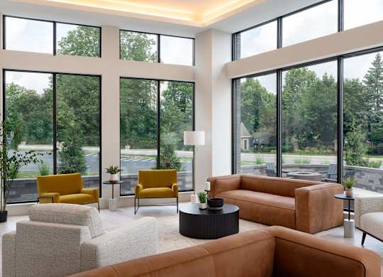 A living room with a large window and a view of trees and a parking lot.