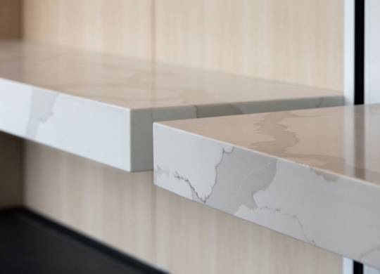 A close up of a white marble shelf with a wooden background.