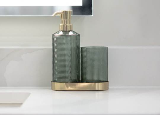 A gold soap dispenser with a green pump sits on a white countertop.