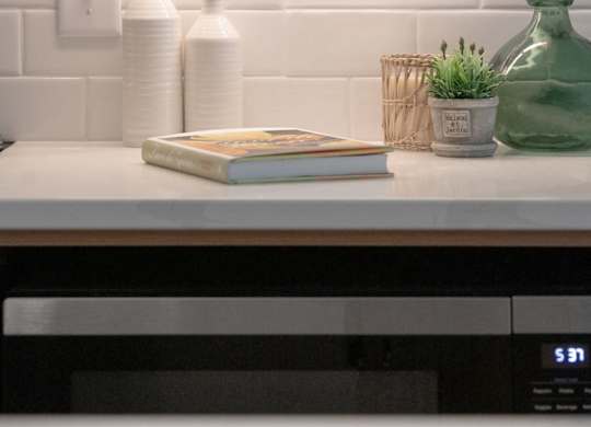 A kitchen counter with a book, two bottles, and a green vase.